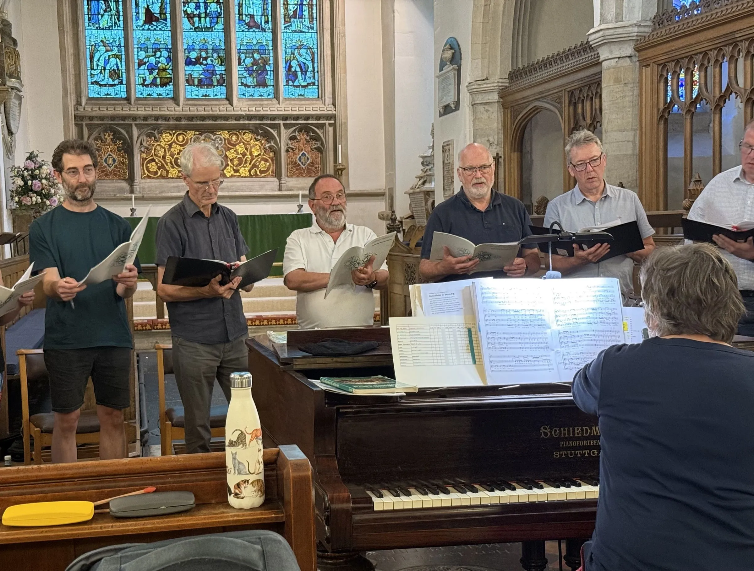 The musical director conducting from the piano, with tenors and basses singing